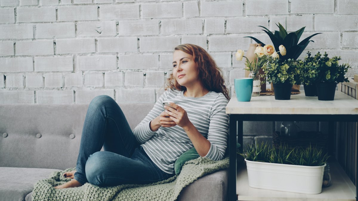 Mieterin entspannt mit Smartphone und Kaffee auf dem Sofa